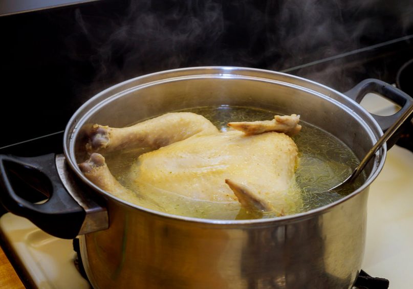 Chicken soup or broth with whole ckicken in the pot.
